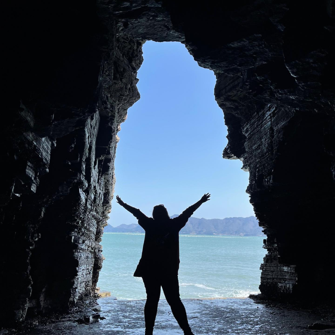 An ETA stands silhouetted in a cave opening that opens to blue ocean.